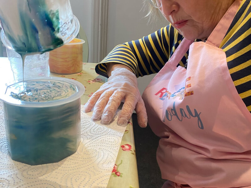 Mum pouring paint into plastic cup to create resin art plant pot